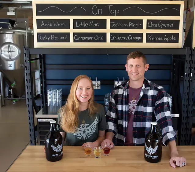 Kenneth and Denise smiling serving their cider, in sample glasses and growlers togo.